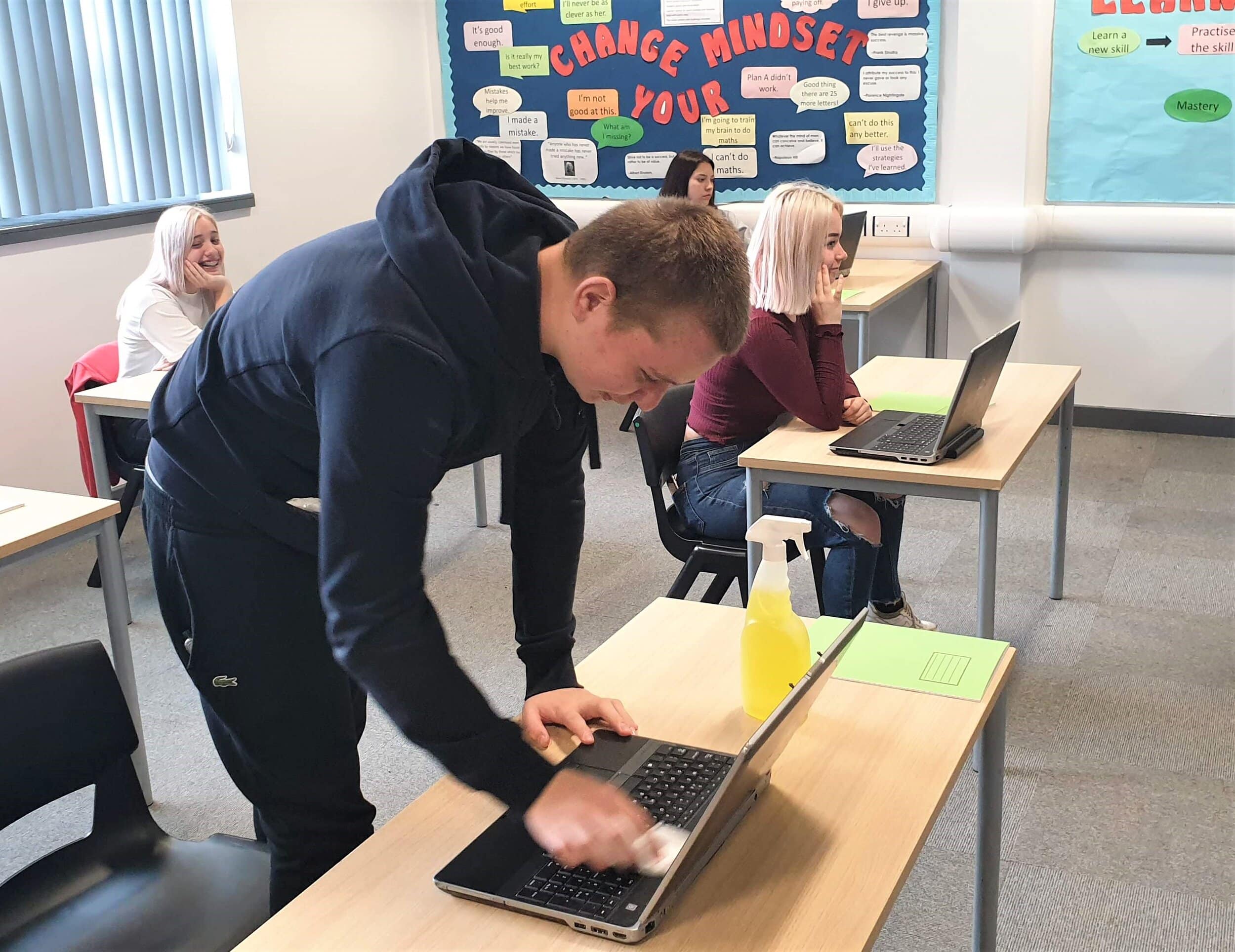 Student Max Gee wipes down his laptop with antibacterial spray. Students are issued with equipment and are not allowed to take it home, and must clean their laptops before leaving for the day.