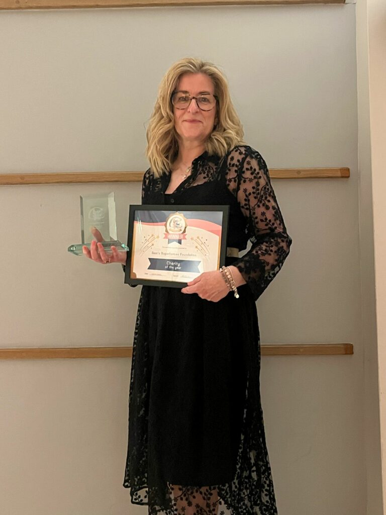 Rachel Liew the founder of Sam's Superheroes Foundation standing in front of a wall holding her award