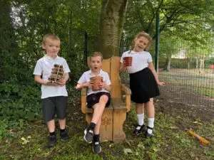 Three children standing and sitting under trees in a school's forest area.