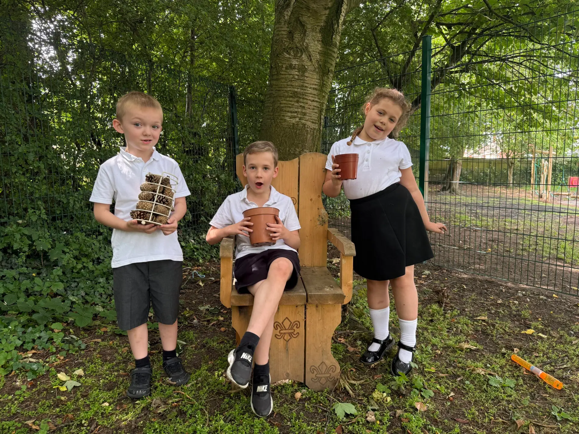 Three children standing and sitting under trees in a school's forest area.