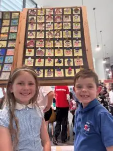 Two pupils smile beside a display of their classmates' self-portrait artwork at the Derby Diocesan Academy Trust art exhibition celebrating creativity.