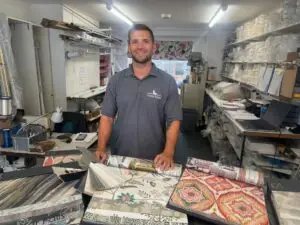 Myles Hayhurst stands in the Castle Blinds office behind a table showing a range of soft furnishings.