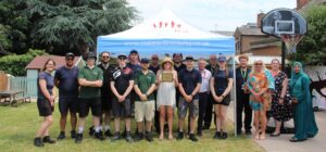 A team of apprentices stand beneath a Children First Derby gazebo holding a plaque. They are stood within a bright and colourful playground.