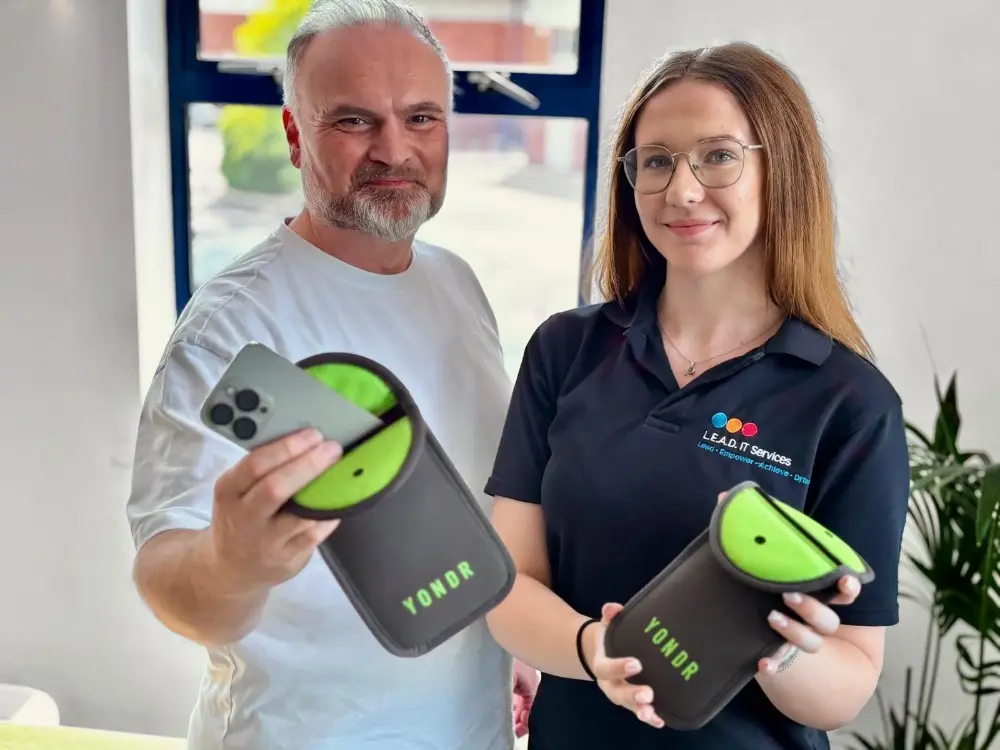 L.E.A.D IT Services staff members hold Yondr phone pouches, demonstrating the secure phone-locking system.