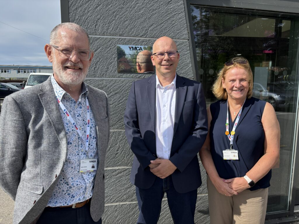 Julian Smith, Matt Jones and Gillian Sewell stand outside a YMCA Derbyshire building, smiling for the camera.