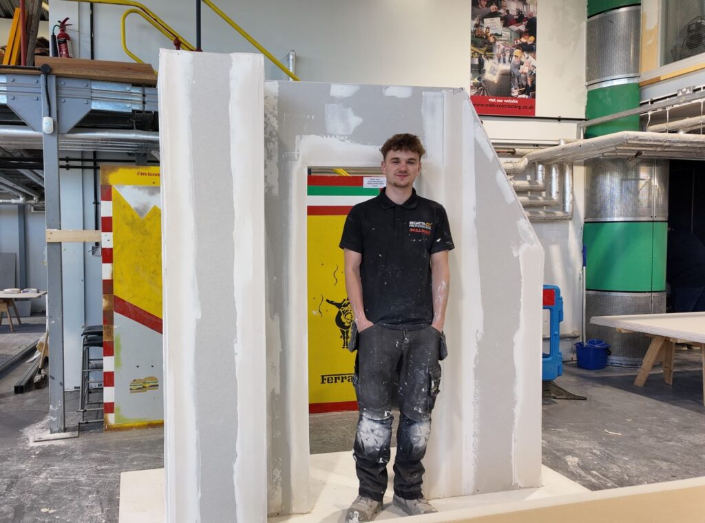 Harrison Priestley stands beside his completed drylining project at the SkillBuild Regional Finals.