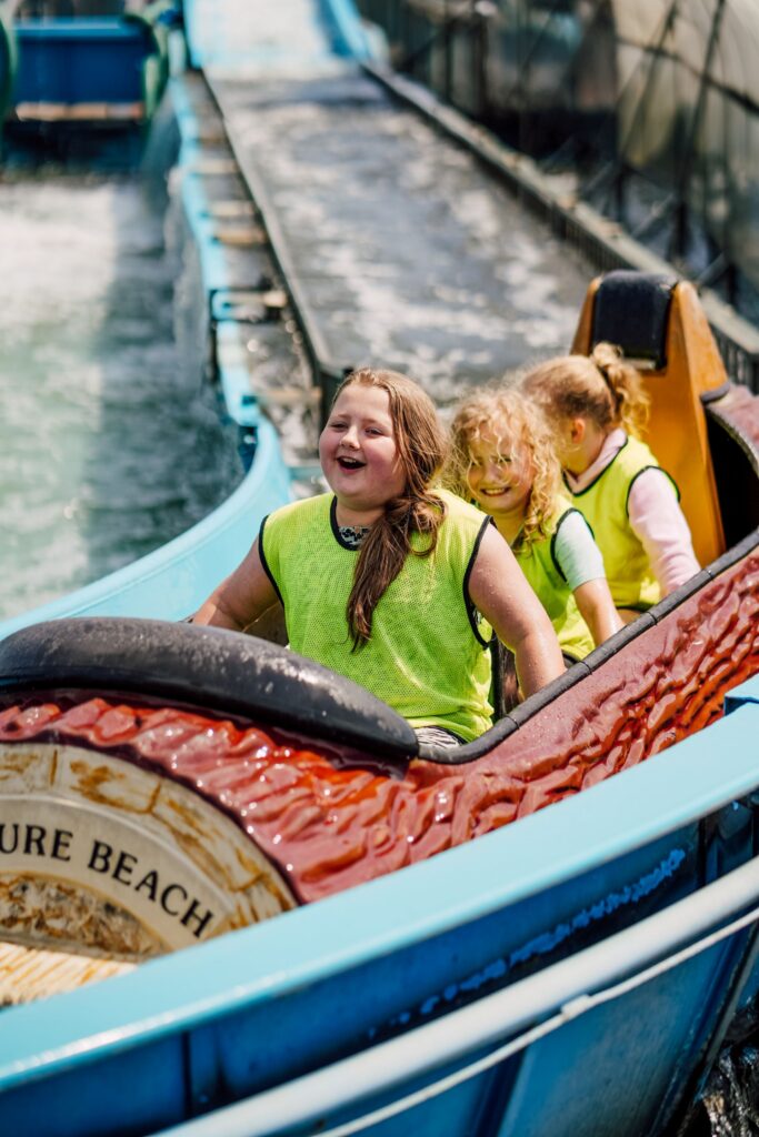 Children wearing high-visibility vests enjoy a water ride during a day out at a seaside theme park as part of a Derbyshire Children's Holiday Centre trip.